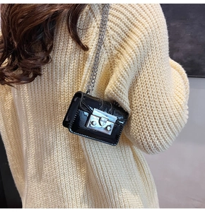 Detail shot of mini black patent leather crossbody bag with silver chain on model
