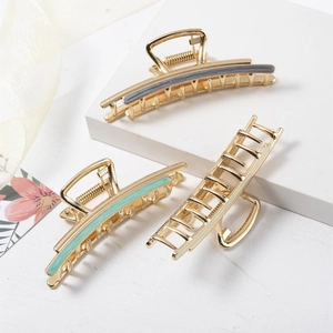 Three elegant gold metal hair clips with enamel accents on a clean white display stand