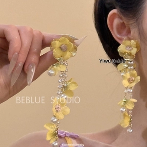 Gros plan sur de longues boucles d'oreilles fleurs jaunes en tissu avec perles