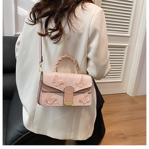 Close-up of pink handbag featuring detailed butterfly embroidery and woven chain handle