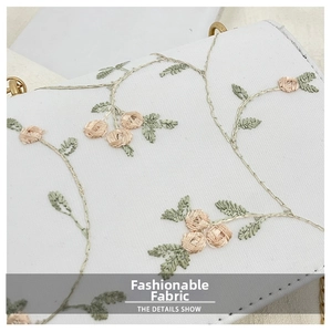 Close-up of white canvas bag with delicate floral rose embroidery and gold chain details