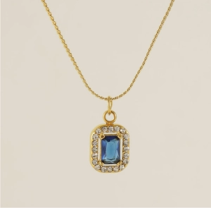 Close-up of golden square pendant with blue rectangle zircon and pavé diamond halo