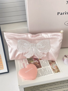 Pink satin cosmetic bag featuring large white bow embroidery and a pearl zipper pull