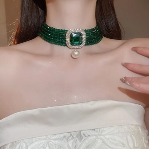 Detail of vintage choker featuring green crystals and a pearl pendant on a model's neck