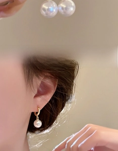 Detail view of large white pearl earrings with gold hoop clasp and model wearing style