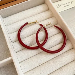 Elegant wine red enamel hoop earrings with gold accents on a beige jewelry display box