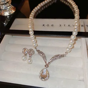 Elegant pearl necklace and teardrop crystal earrings set in a white velvet jewelry box
