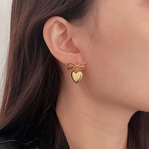 Elegant gold bow earrings with heart drop pendant worn by a model for a stylish look