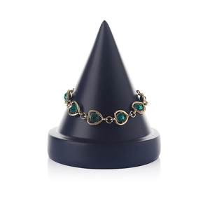 Close-up of golden bracelet with green heart gemstones on a black cone jewelry stand