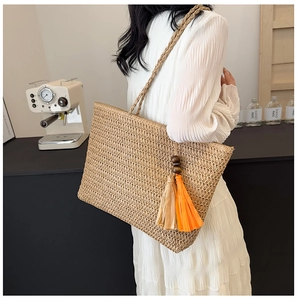 Detail of straw tote bag with orange and beige tassel charms and woven handle