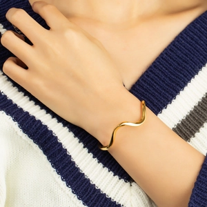 Elegant gold wavy open bangle bracelet for women styled on a soft knit sweater