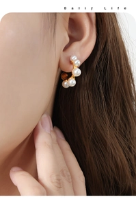 Close-up of elegant C-shaped gold earrings with five white pearls on model's ear