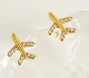 Détail de boucles d'oreilles avion dorées serties de diamants sur fond glacé