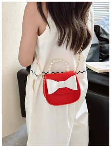 Detail of red crossbody bag featuring pearl handle, white bow, and gold chain strap