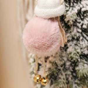 Detail of pink plush Christmas angel ornament with knitted hat and golden bells on a tree