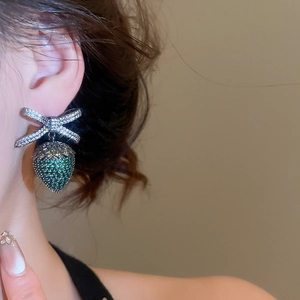 Dettaglio di orecchini vintage a fiocco con zircone fragola verde indossati da una modella