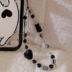 Detail of beaded phone strap with black heart and bear charms on plush background