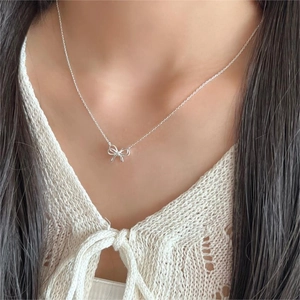 Close-up of minimalist silver bow pendant necklace worn on a model's neck for a delicate look