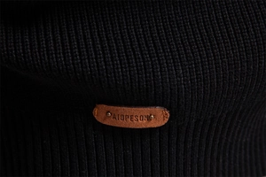 Close-up of brown leather logo patch with metal rivets on black ribbed knit sweater