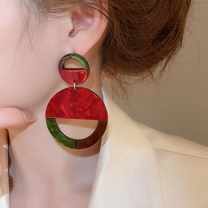 Detail of geometric marble acrylic earrings in red and green worn by a model