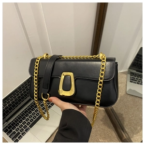 Detail of a black leather handbag with a gold chain strap and D-ring clasp in an office setting