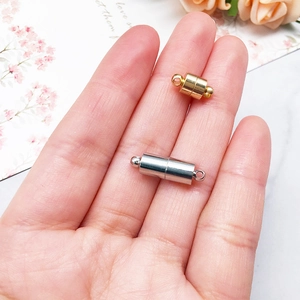 Close-up of golden and silver magnetic jewelry clasps held by hand for scale and detail
