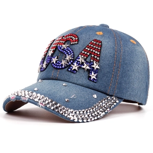 Detailed macro view of the rhinestone-studded USA logo on a distressed blue denim baseball cap.