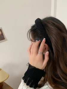 Side view of a black fuzzy headband and silver rings on a model in a cozy home setting