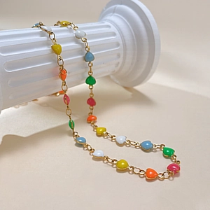 Détail d'un collier plaqué or avec des cœurs colorés en émail sur une colonne blanche