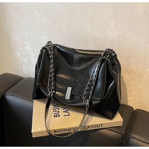 Detail of black glossy leather shoulder bag with silver chain strap on a sofa
