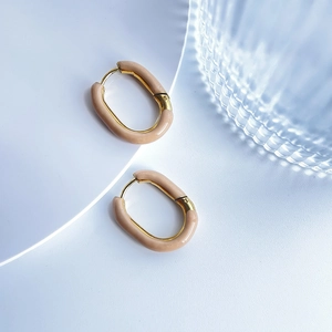 Detailed close-up of oval gold-plated earrings with beige enamel inlay on a clean stand