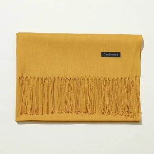 Close-up detail of soft yellow cashmere scarf with elegant fringe texture and label