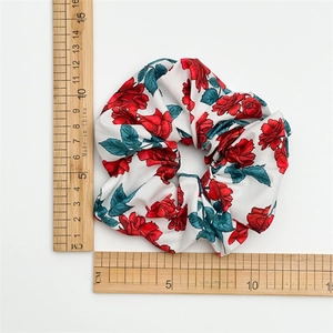 Floral scrunchie with red rose print and leaves shown on white background with scale ruler