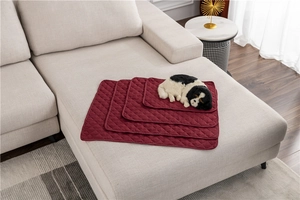 Stack of waterproof wine red quilted pet mats in four sizes displayed on a modern sofa