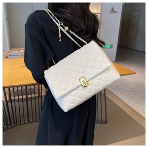 Detail view of white quilted shoulder bag with gold chain strap and turn-lock closure