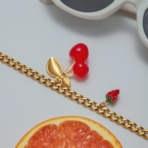 Close-up of gold Cuban chain necklace with red cherry and strawberry fruit charms