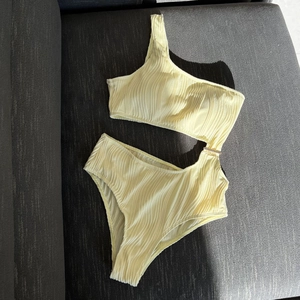 Detail of ribbed yellow swimsuit featuring cut-out waist and gold metal buckle accent