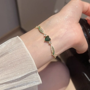 Macro view of emerald heart pendant bracelet with gold twisted rope design and pavé stones