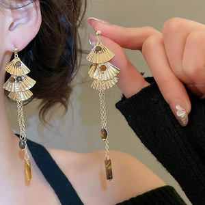 Detail of gold fan-shaped tassel earrings with tiger eye stones and ginkgo leaf design