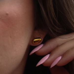 Minimalist polished gold bean earrings in oval shape worn by model in a stylish setup