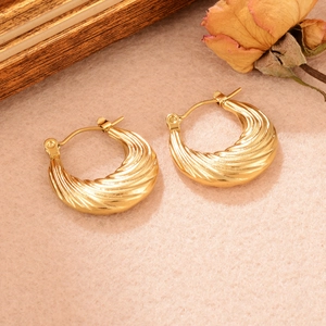 Gros plan de boucles d'oreilles dorées torsadées en U sur un fond esthétique vintage