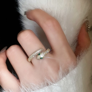 Close-up of a gold-plated snake ring with pavé zircons and green emerald-eye accents
