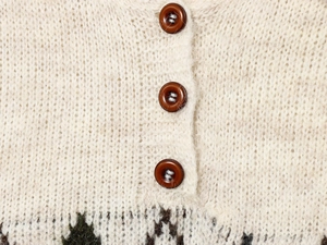 Detail of cream chunky knit cardigan with resin buttons and geometric jacquard pattern