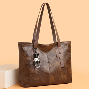 Brown textured leather tote bag with bear pendant charm on a soft warm background