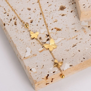 Elegant gold butterfly necklace with triple pendants and bead accents on stone surface