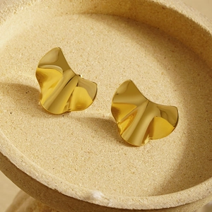 Boucles d'oreilles dorées irrégulières en forme de ginkgo sur un plateau minimaliste