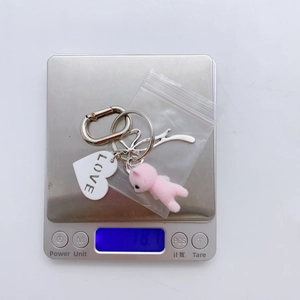 Detail shot of a heart charm keychain with pink plush bear on a scale weighing 18.1 grams