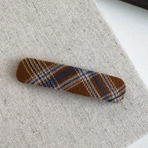 Detail of blue and brown checkered fabric hair clip on beige rustic linen background