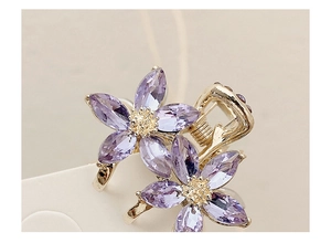 Macro shot of gold metal hair claw with two purple crystal flower designs and rhinestones