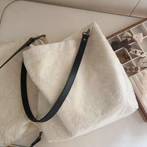 Beige floral embroidered cotton tote bag with black leather strap in flat lay view